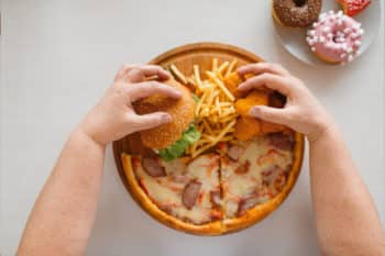 Man's arm and hand on hamburger, pizza, french fries, with donuts near by