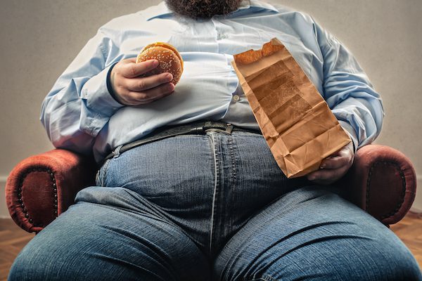 Middle,Aged,Man,Snacking,In,An,Armchair, sedentary obese fast food, overeating, addiction