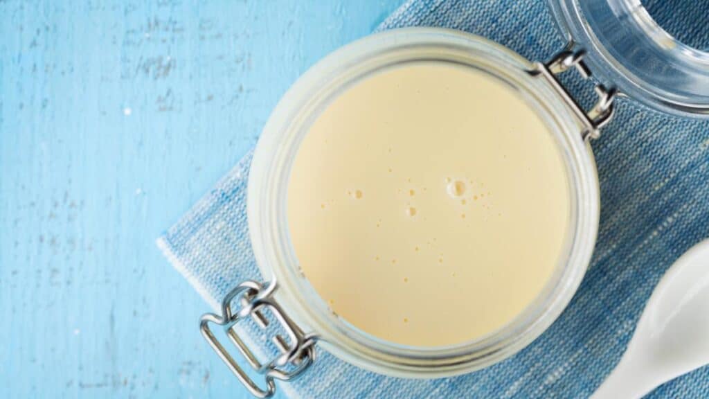 Jar with condensed milk or evaporated milk on blue table top view