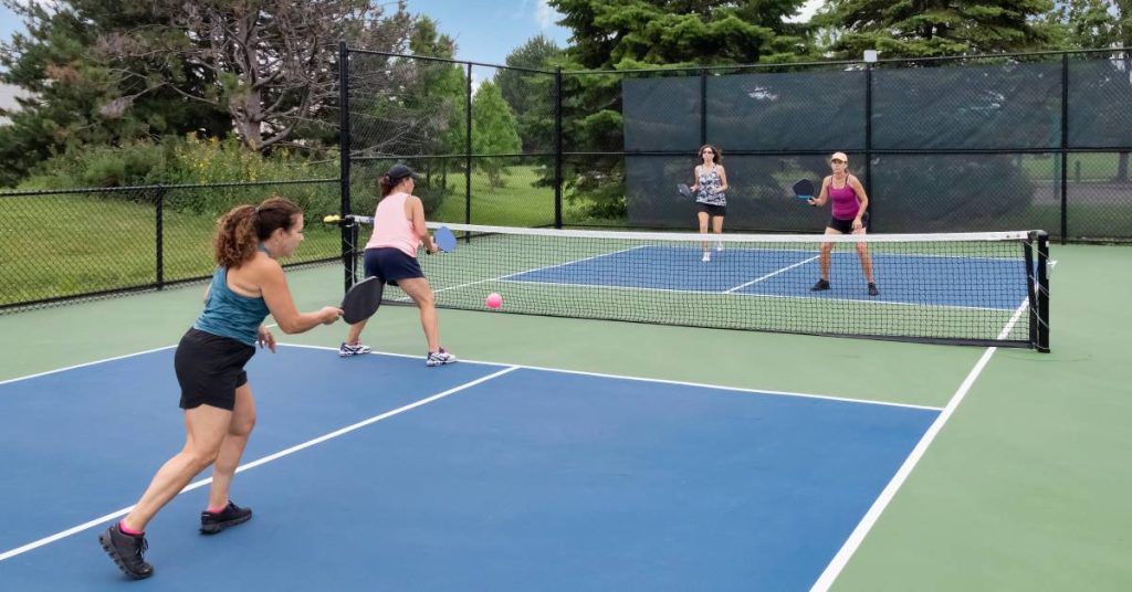 A pickleball court with two teams of doubles playing a match. Two players are close to the net and the others in the back.