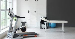 A small home gym with a few pieces of equipment. There's a manual treadmill and a massage table on the side.