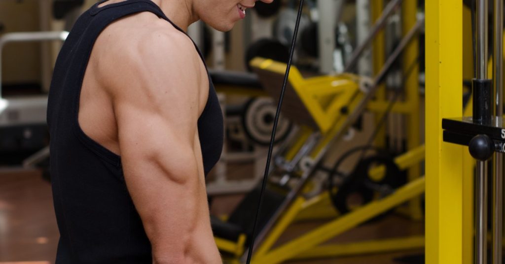 A young adult using a gym cable machine to pull down a grip. The machine’s weight stack has two plates engaged.