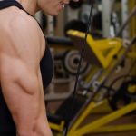 A young adult using a gym cable machine to pull down a grip. The machine’s weight stack has two plates engaged.