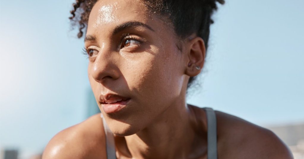 A young person with bright brown eyes staring into the distance. They are sweating and wearing athletic gear.