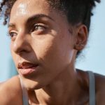 A young person with bright brown eyes staring into the distance. They are sweating and wearing athletic gear.